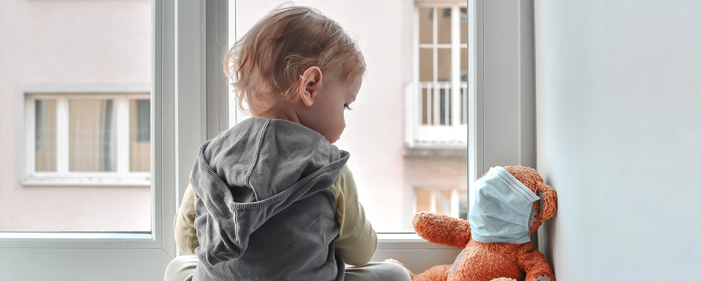 A baby looks at a teddy with a face mask